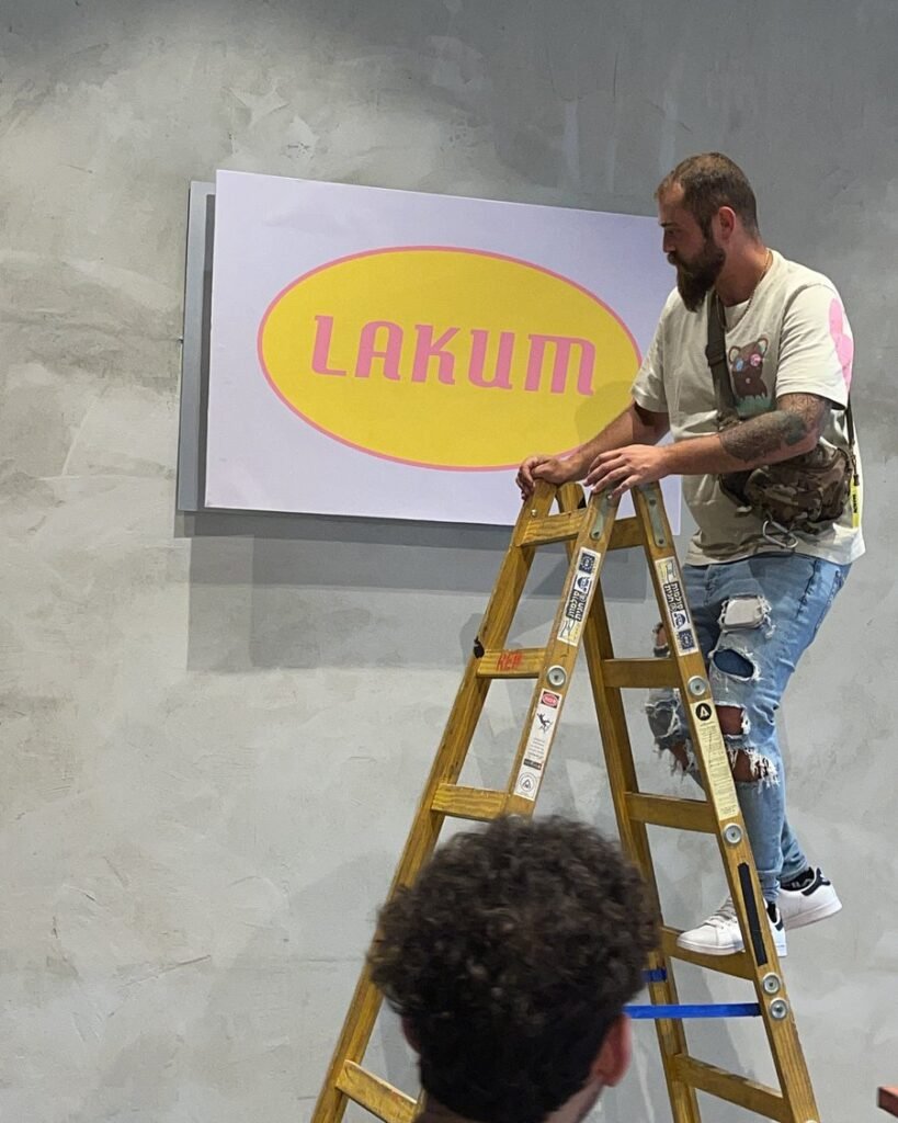 אדיר קדישא על סולם תולה את שלט LAKUM על קיר הסט